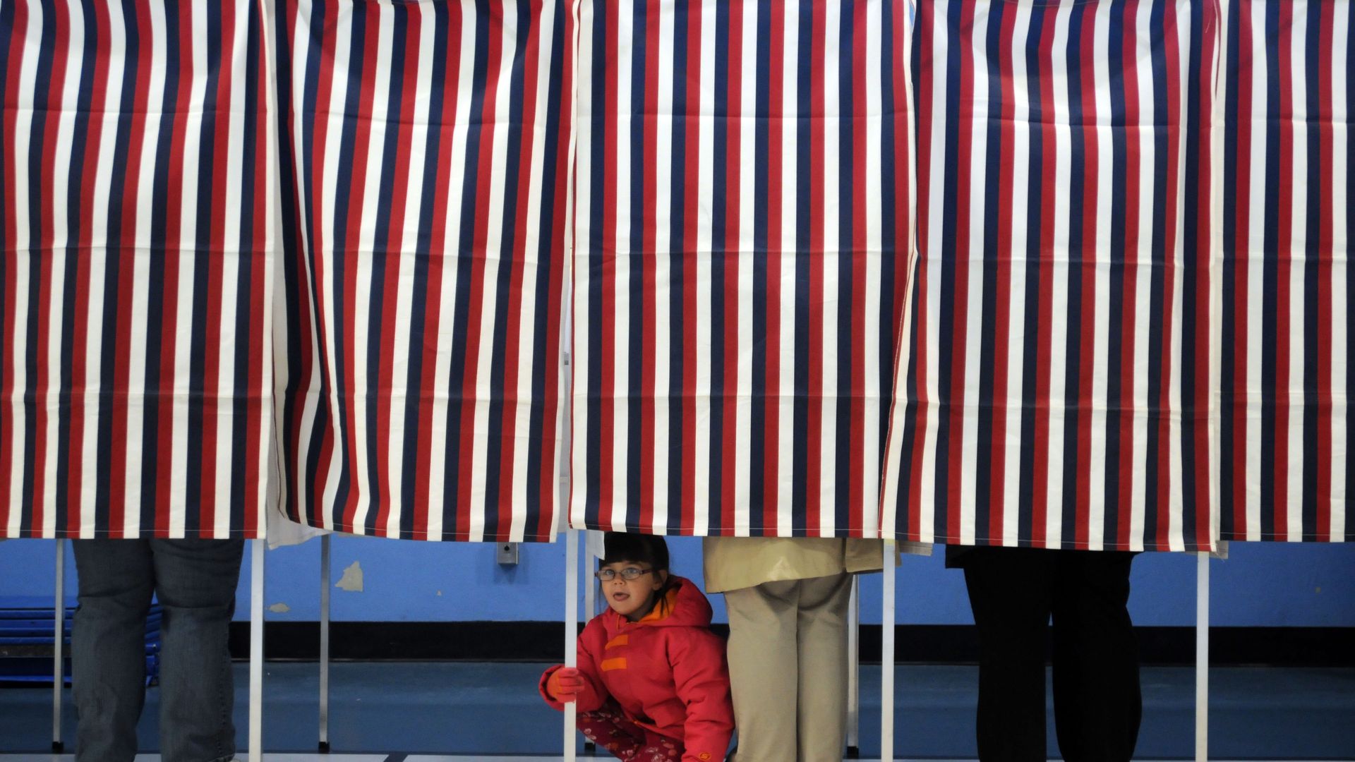 Poll booths with red, white, and blue curtains, while people vote.