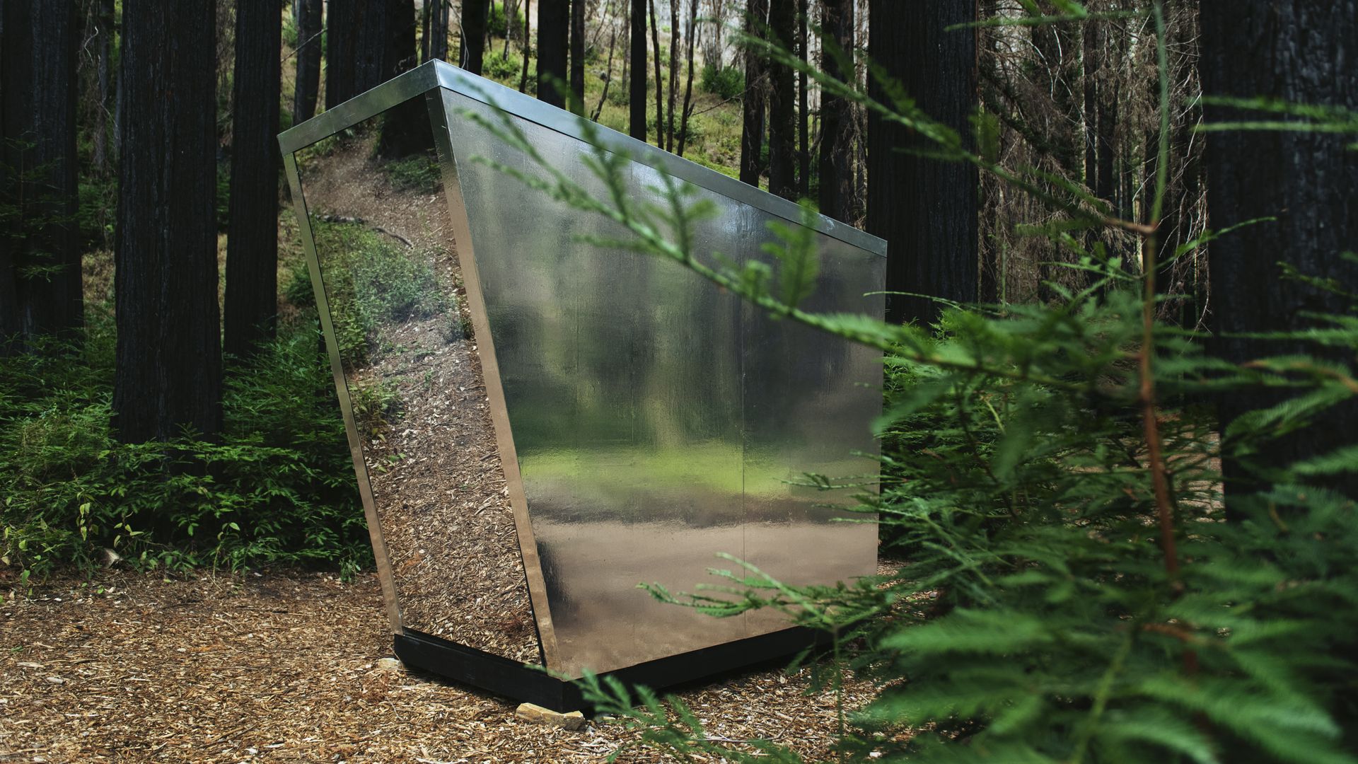 The Portal, a futuristic-looking mirrored outdoor toilet, sitting in a forested area.