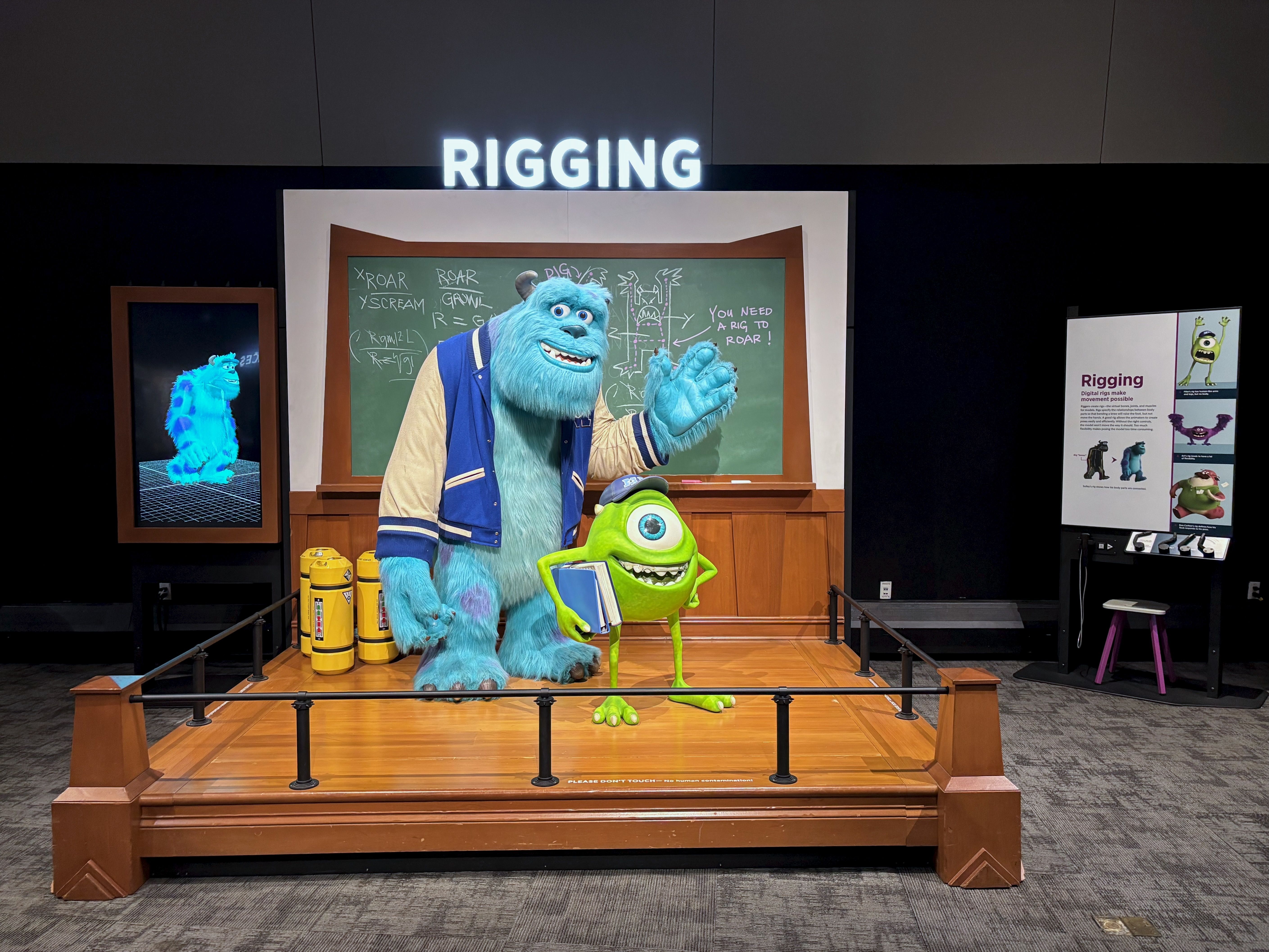 Display featuring blue fuzzy Sulley and green one-eyed Mike from "Monsters, Inc." in front of a chalkboard labeled RIGGING with sketches and text about rigging cartoon characters.