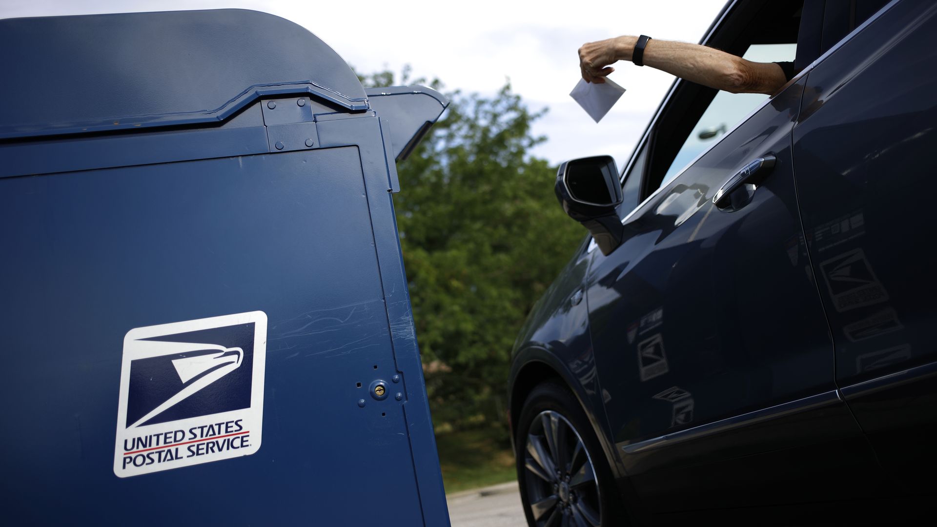 A motorist drops a letter into a United States Postal Service mail drop box.