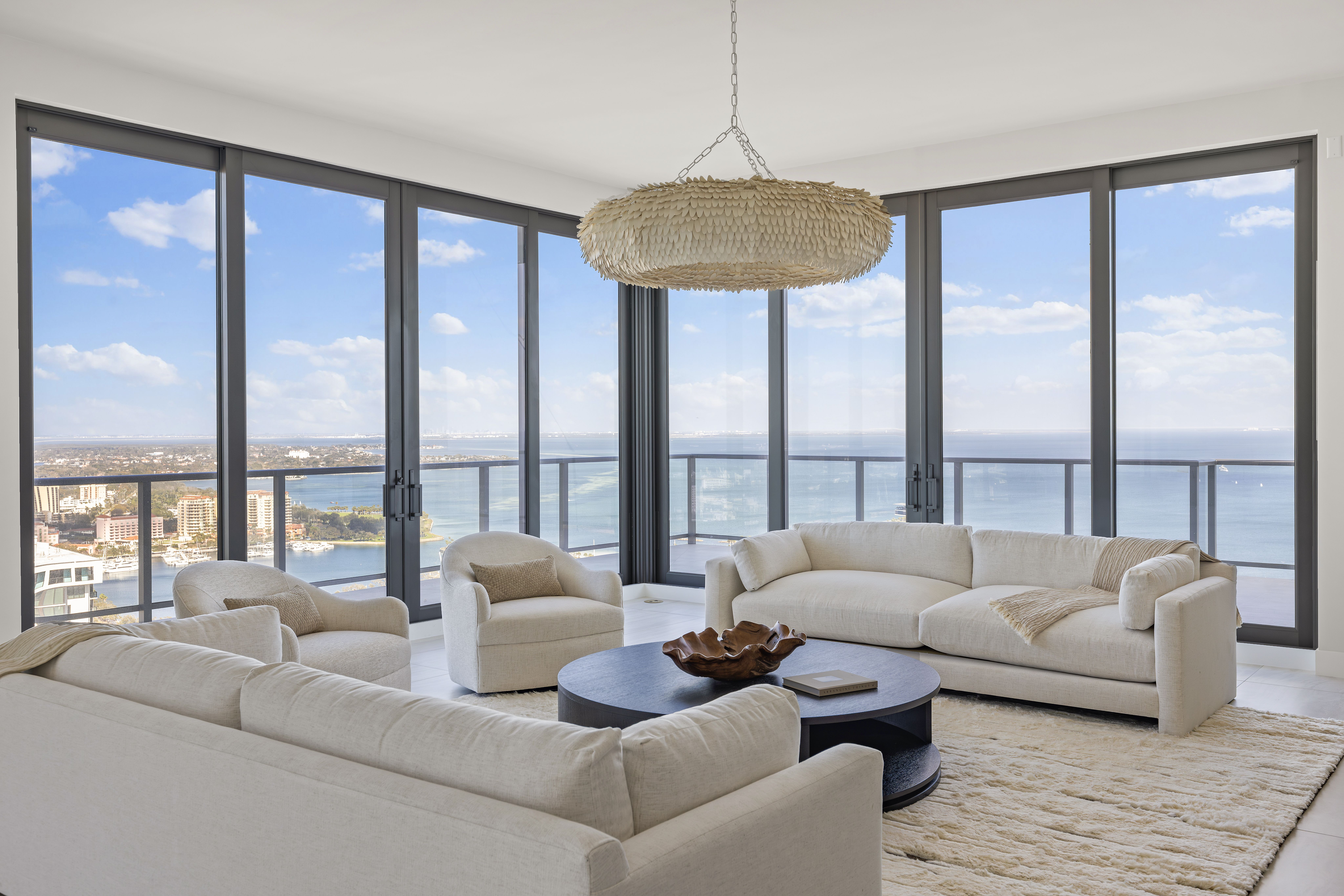 A living room with white sofas and floor-to-ceiling windows with a view of blue water.