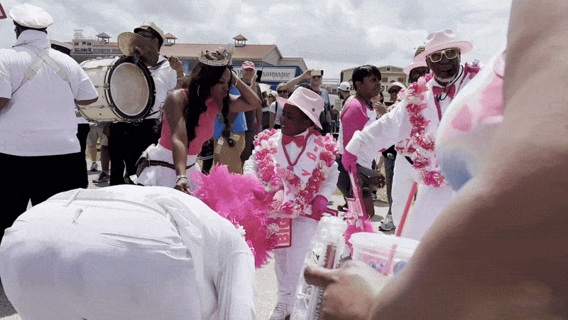 A moving image of the Original Big 7 second-line at Jazz Fest. A young boy, wearing a white suit with pink flowers, dances.