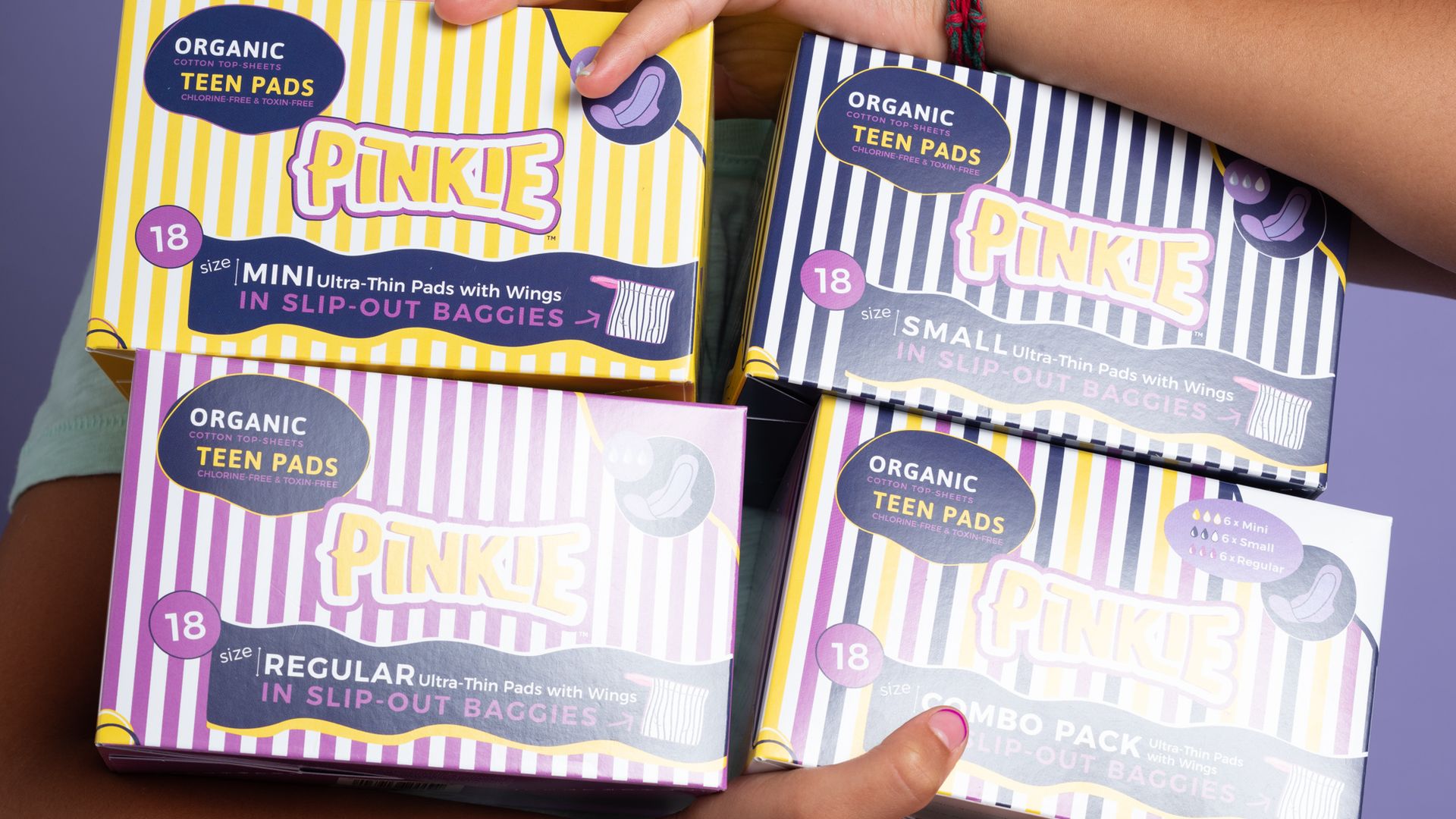 A teen girl holds four different versions of Pinkie-branded period pads.