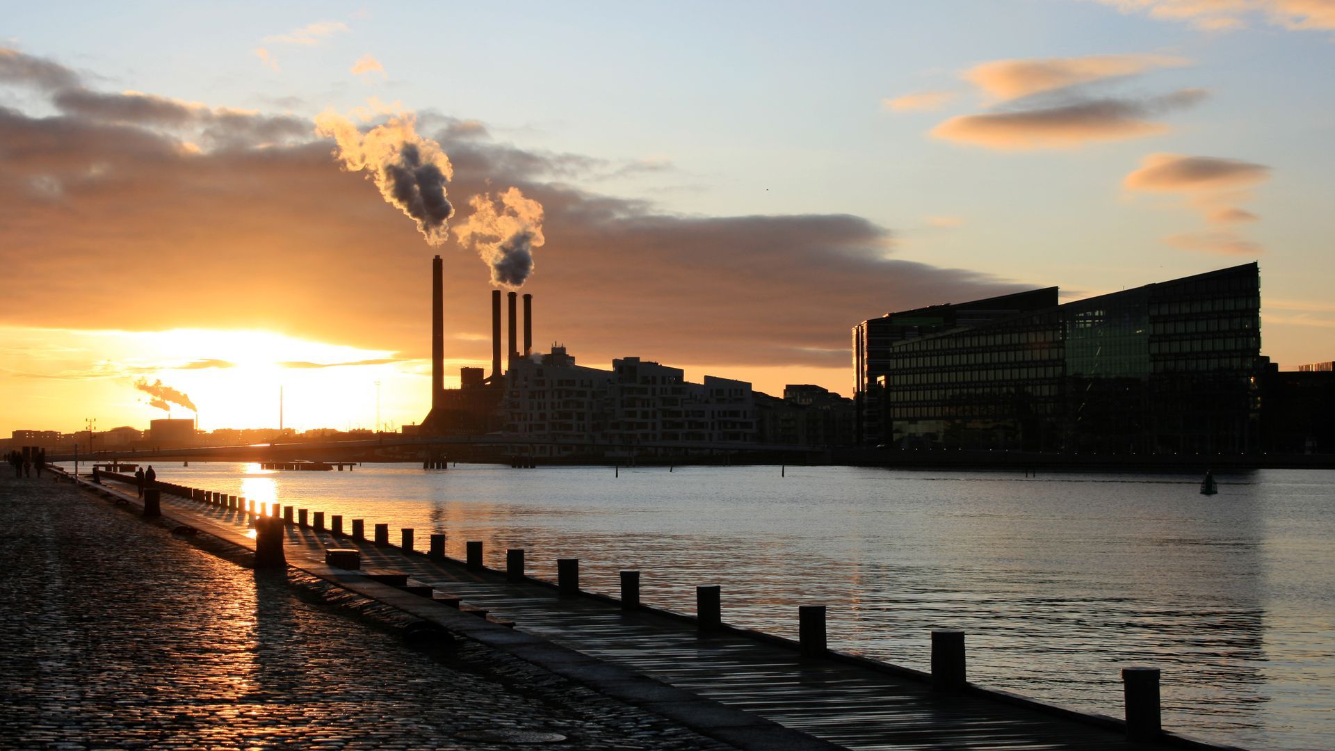 Ørsted Power Station, situated at Sydhavnen in Copenhagen, with the sun rising behind it and the river flowing in front of it