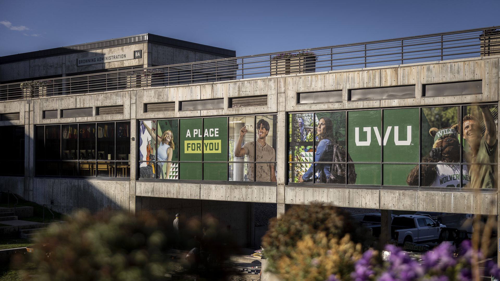 Concrete building with large windows displaying a green banner reading "A PLACE FOR YOU" and "UVU" alongside images of smiling students and a mascot in UWU Wolverines gear.