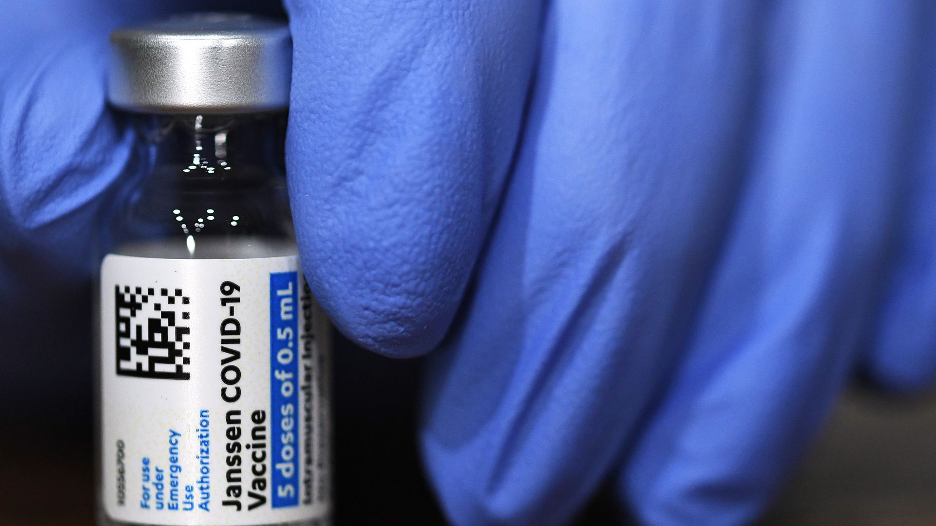 A blue glove holds a vial of the J&J COVID-19 vaccine.