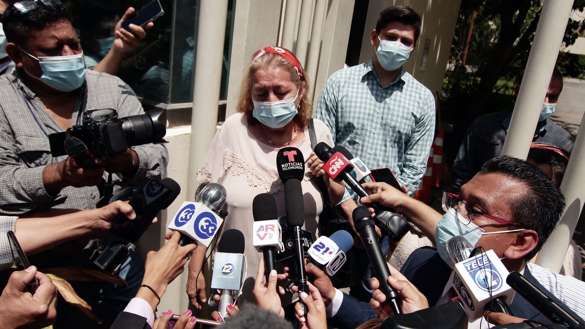 Photo of a masked person with a horde of microphones pointed at her