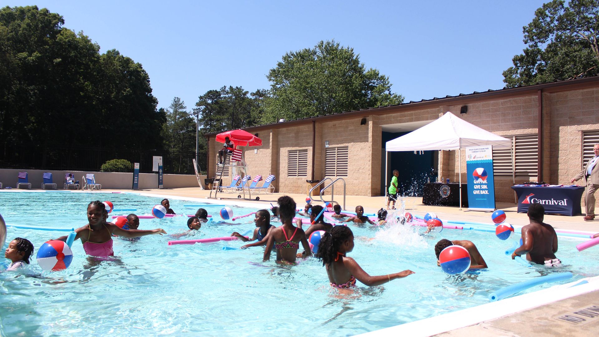 A photo of children playing in an Atlanta pool on a bright sunny day while a lifeguard watches from a high chair