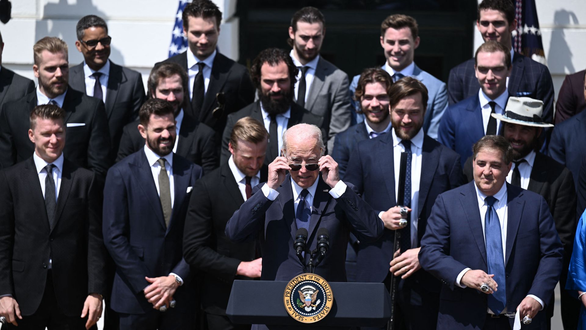 Joe Biden lifts down his sunglasses as members of the Lightning stand behind him in suits