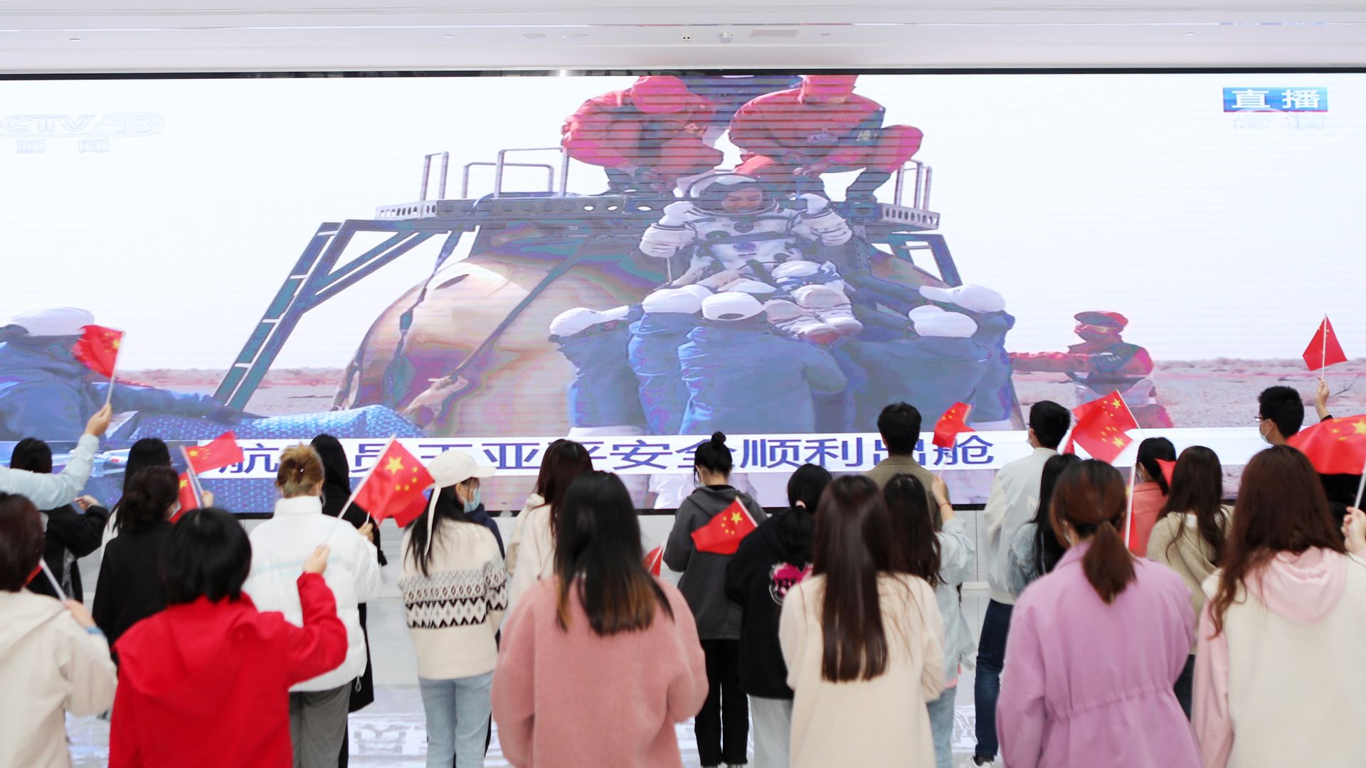 Students wave Chinese national flags as they watch a live TV broadcast of the landing of Shenzhou-13 return capsule.