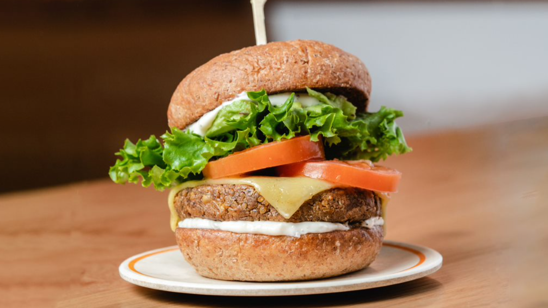 A burger on a bun with tomato and lettuce and a stick in the middle.