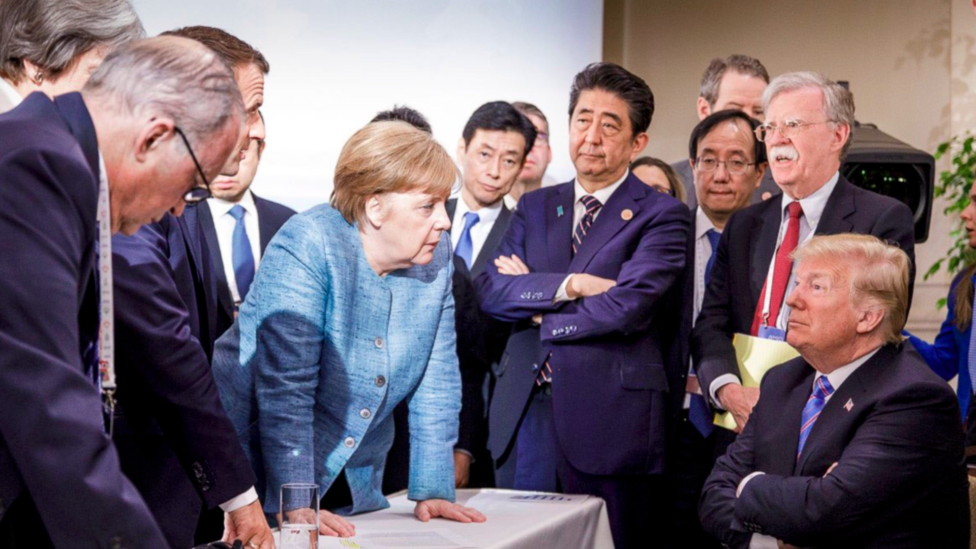 Merkel leans over a sitting Trump
