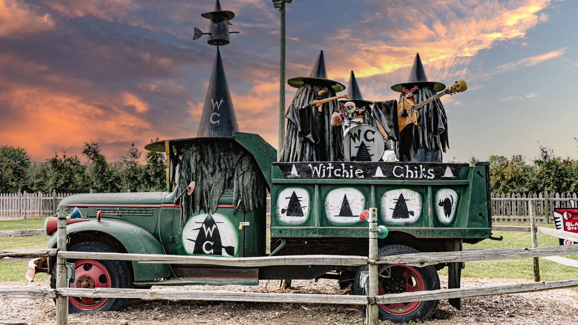 Green truck turned into a Halloween display with black drapes, tall cone hats, skulls and bones, a guitar, and a sign.