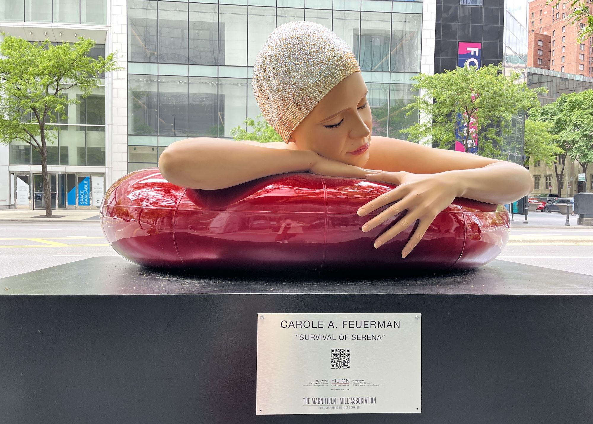 A sculpture of a woman on a red inner tube wearing a swim cap with crystals