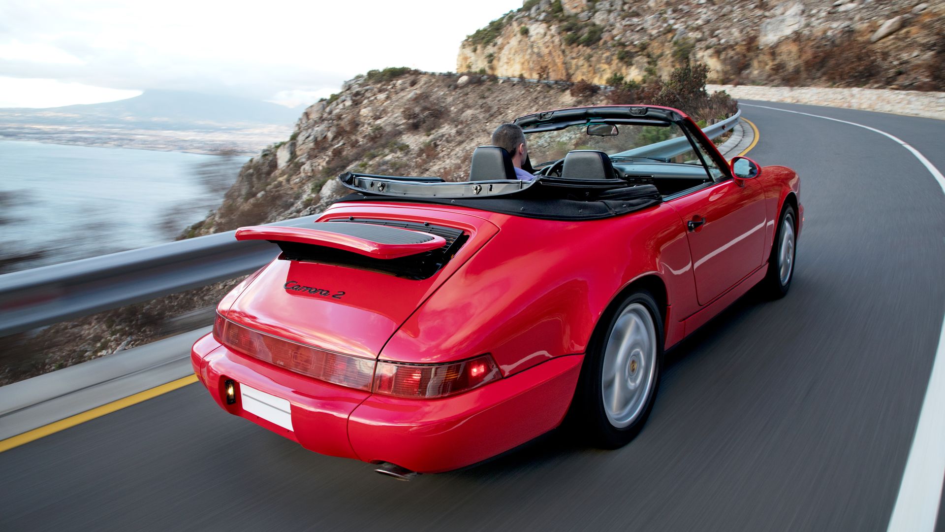 Photo of a red Porsche on a winding road overlooking the ocean