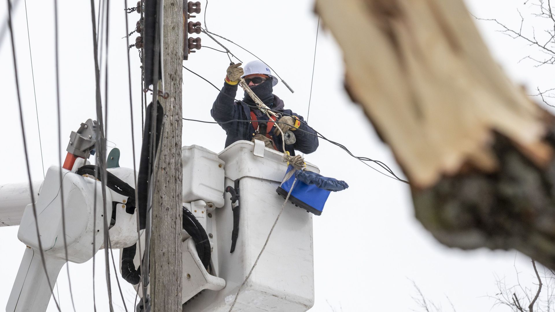 A DTE worker shown from below, up working on electrical wiring along a telephone pole.