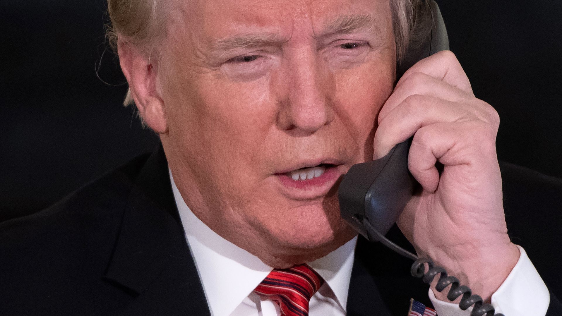 A close-up image of then-President Donald Trump with a landline phone receiver to his left ear.