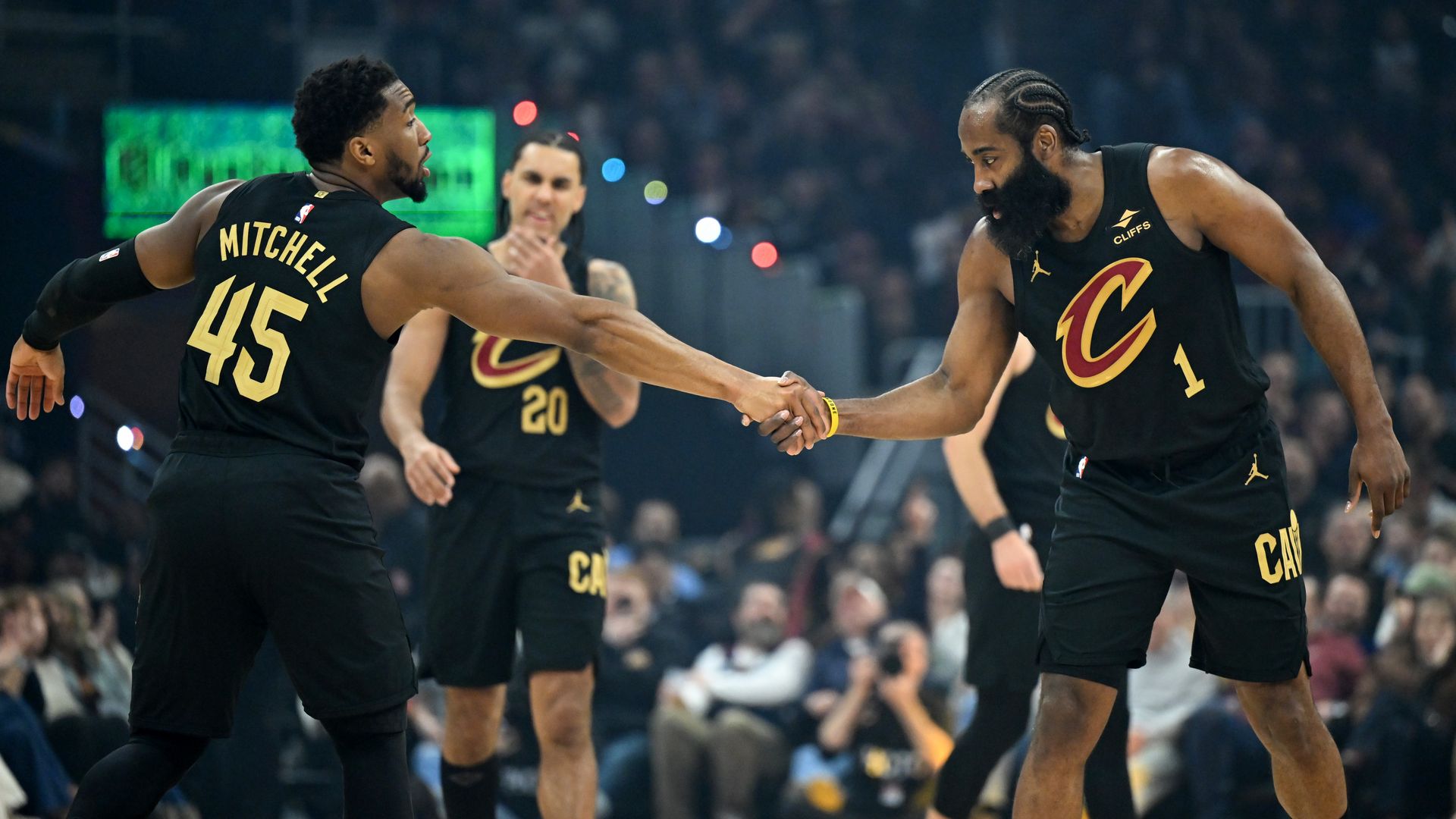 Donovan Mitchell in black #45 jersey shakes hand of bearded James Harden, also in black jersey with red "C" on front. 