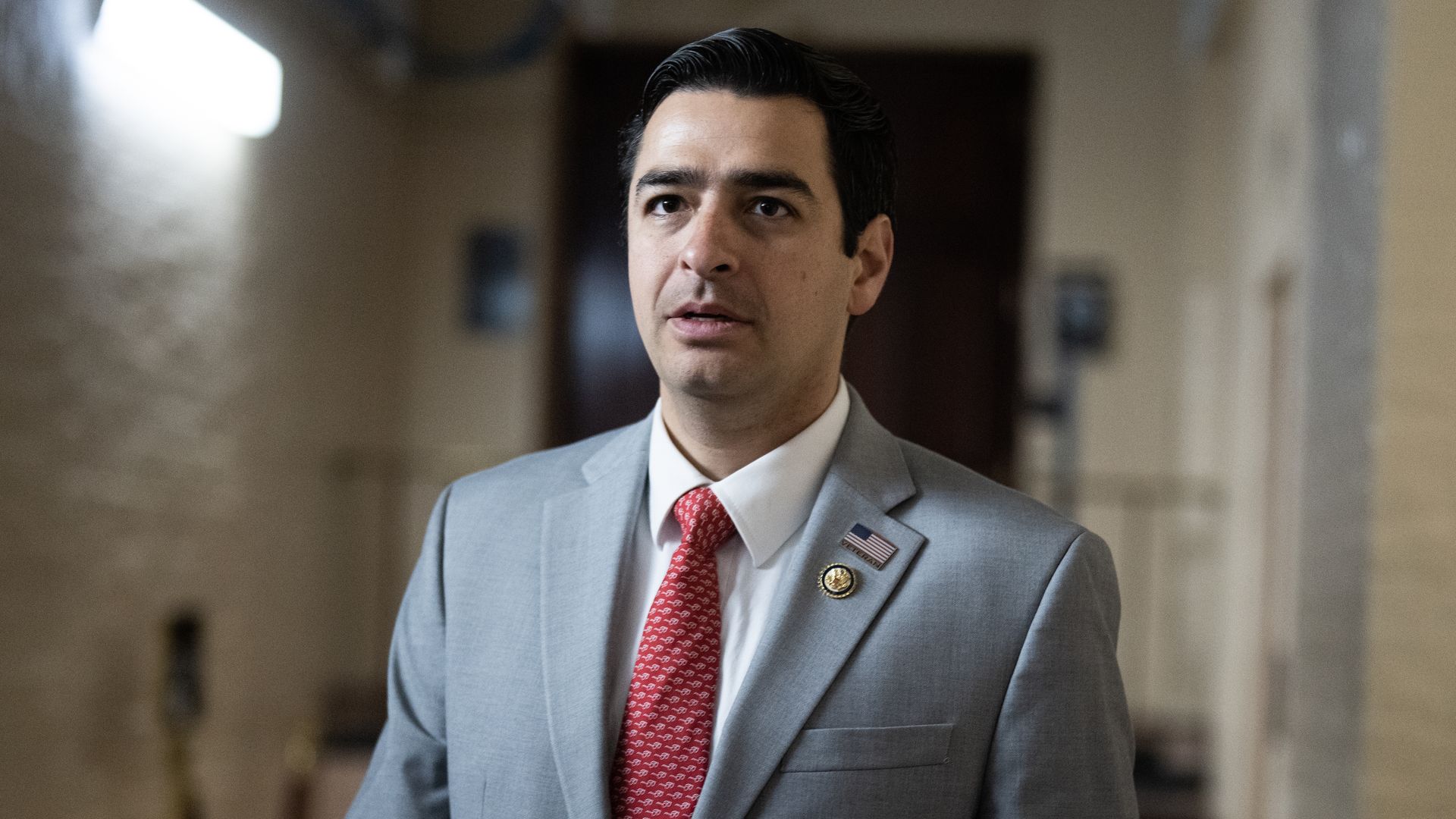 Rep. Gabe Evans, wearing a gray suit and standing in a white brick hallway.