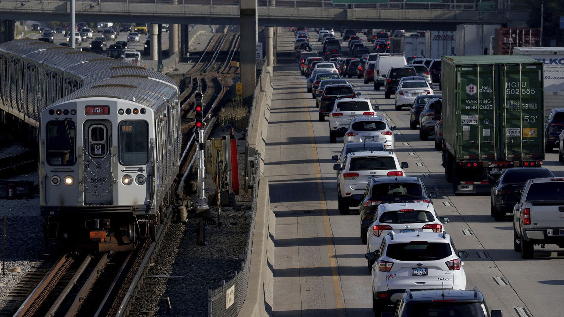 A CTA train on the left next to the expressway where traffic is bumper to bumper.