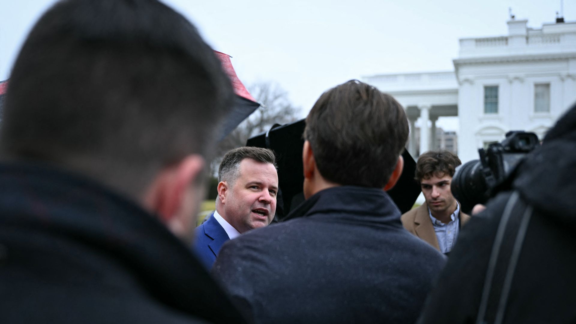 Bill Pulte can be seen talking to multiple reporters outside of the White House while wearing a blue suit jacket and a white collared shirt.