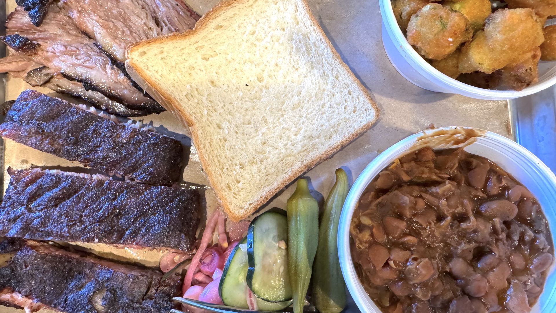 A plate of barbecue — ribs and brisket — surrounding a large piece of white bread. 