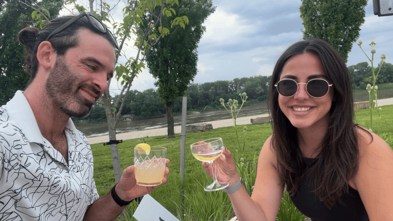 Travis and Abbey clinking glasses with the river and bikers at Berkley Riverfront Park in the background.