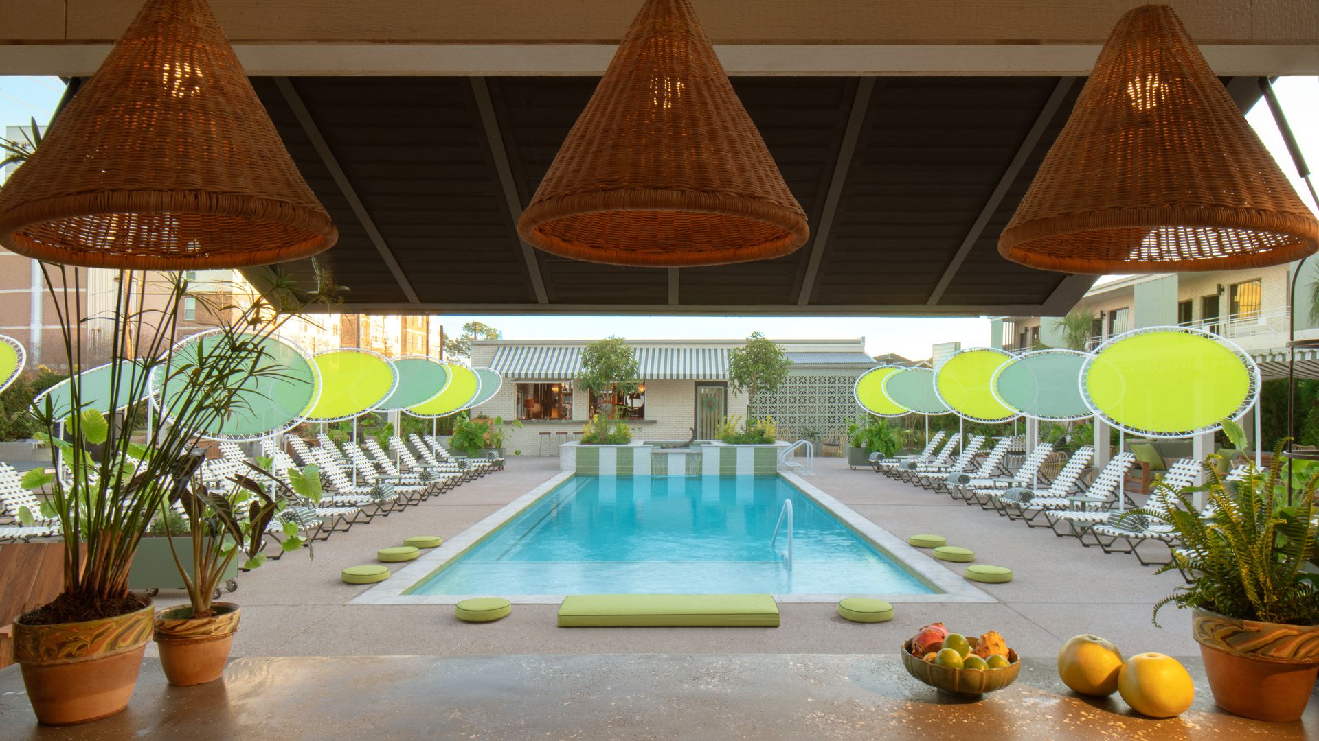 A view of a pool deck from behind a bar, with rattan hanging lanterns overhead.