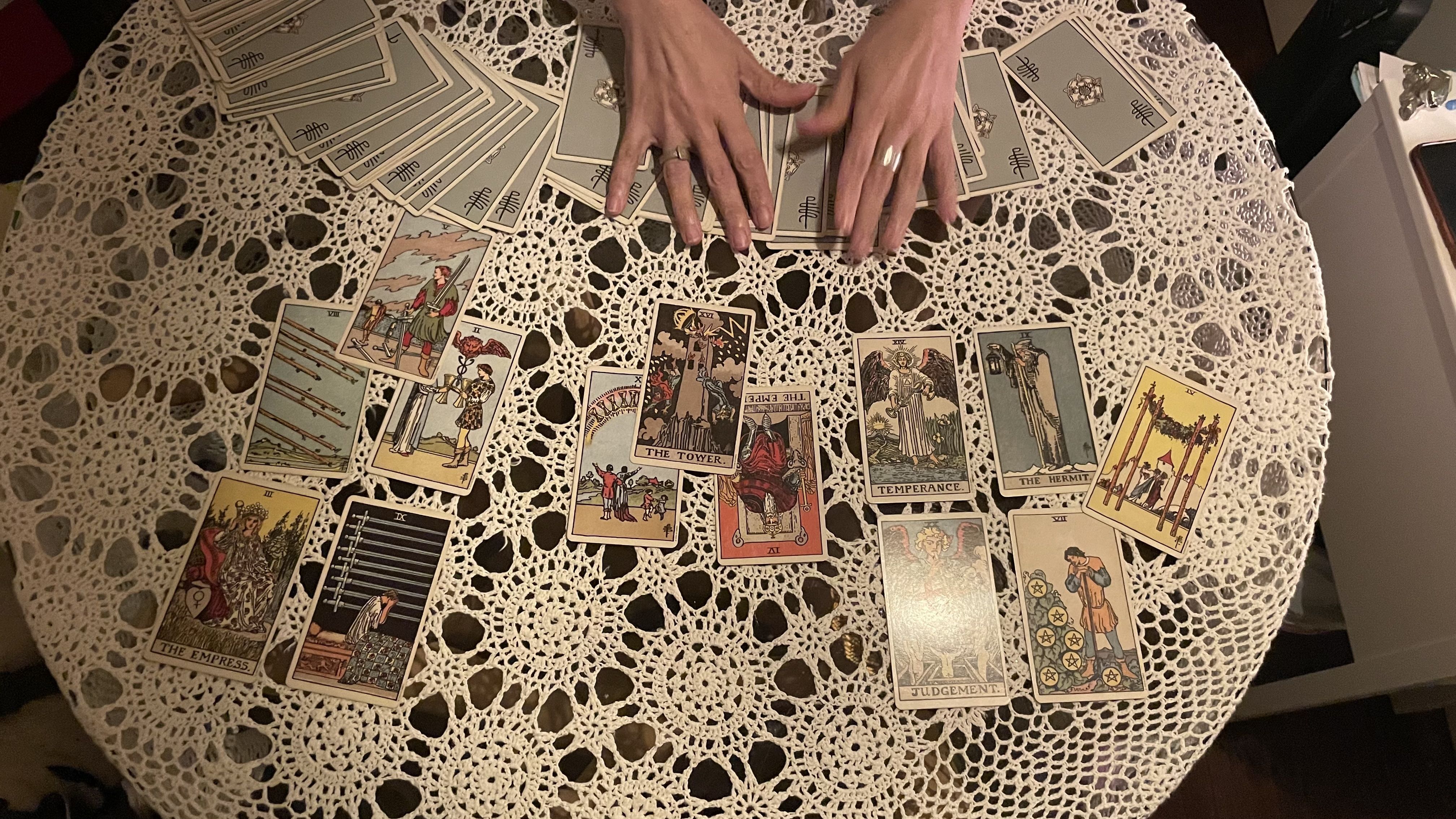 A photo of tarot cards laid out on a circular table with a pair of hands touching the cards.
