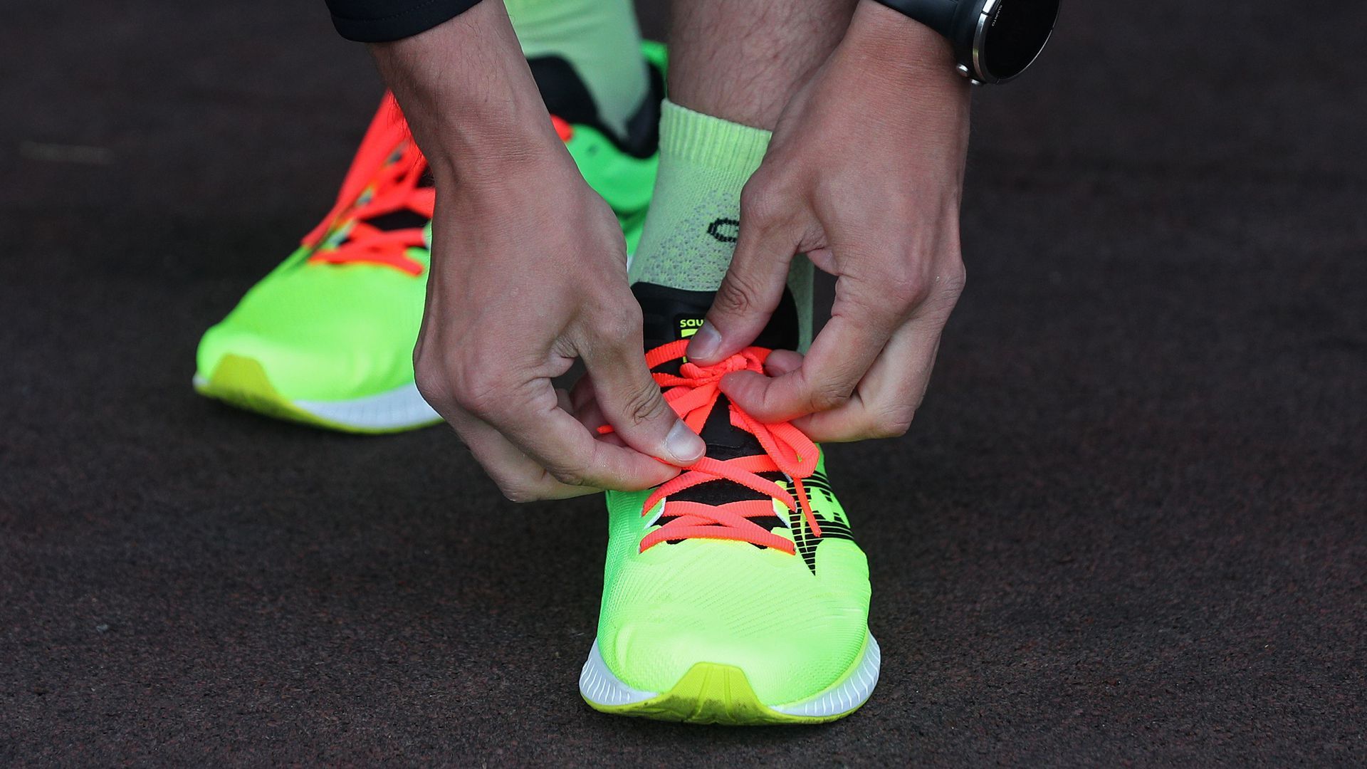 A man's hands lace up neon yellow running sneakers.