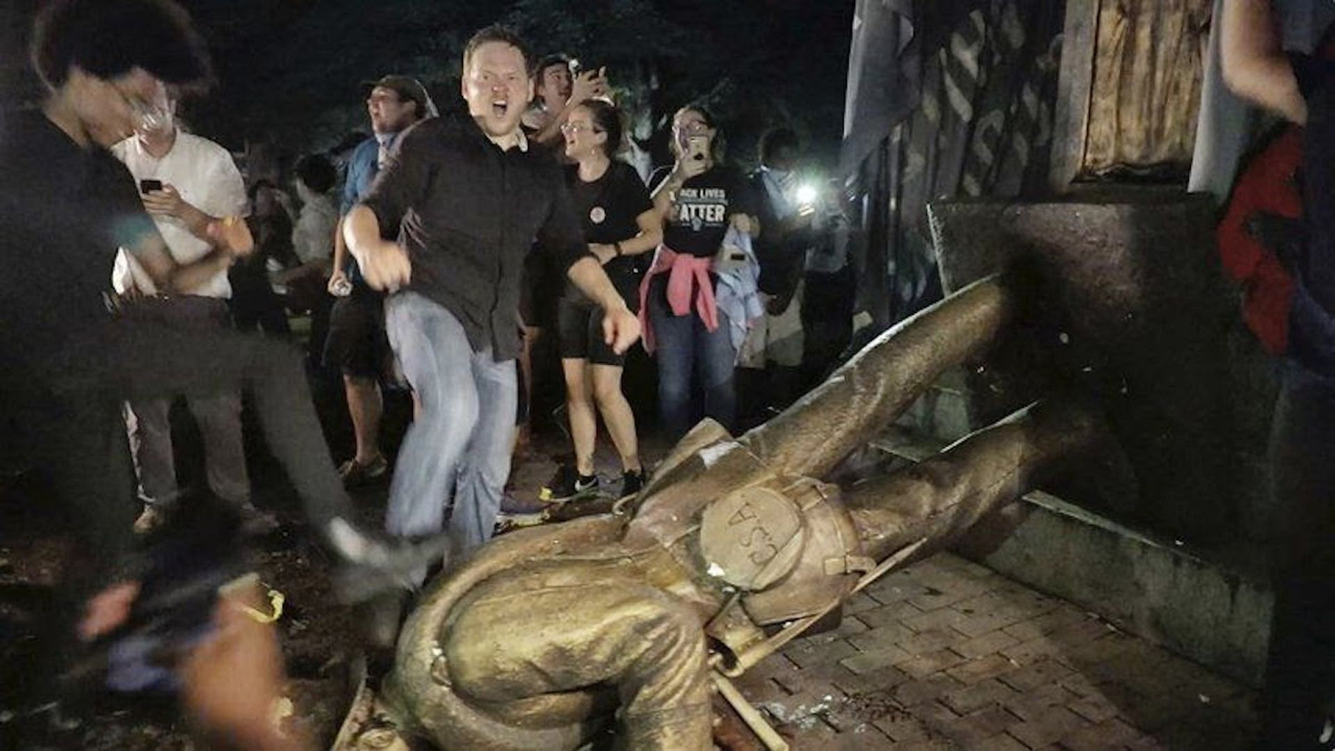 People stand around a fallen statue.