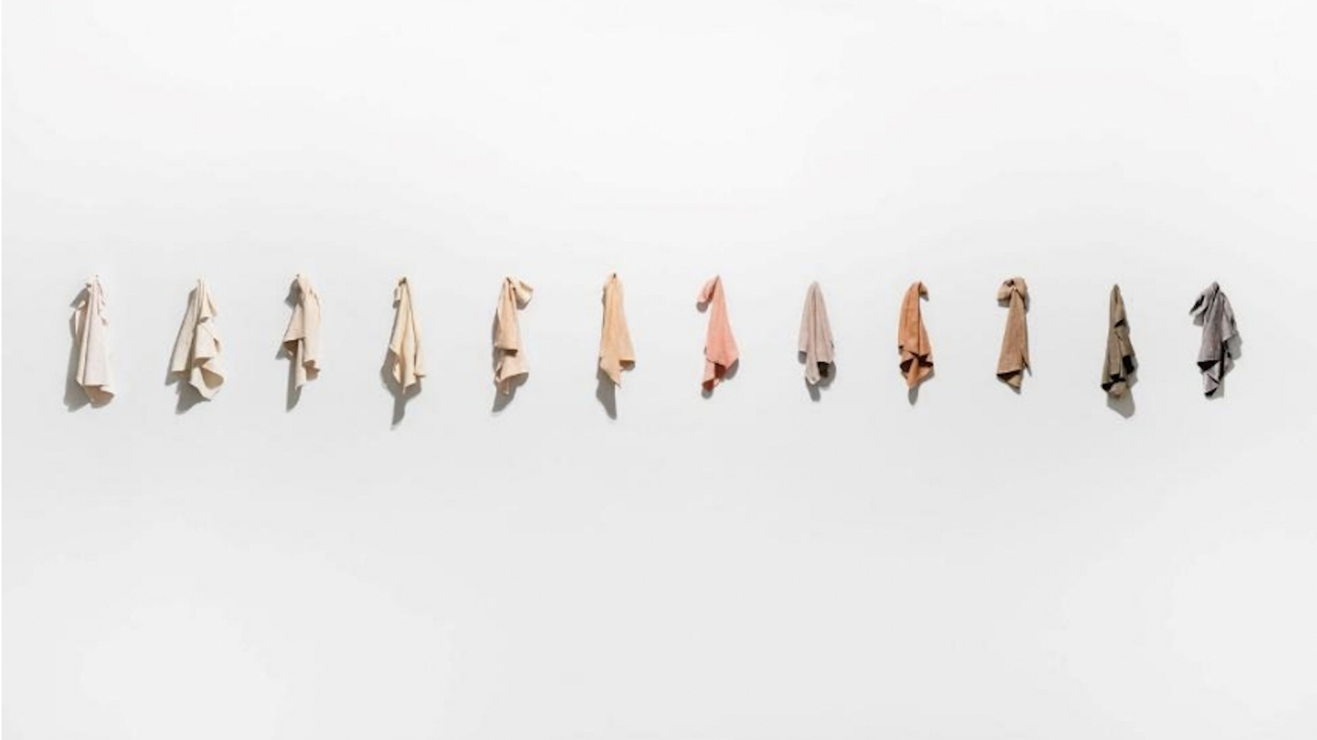 light-colored rags in white, pink and brown pastel hues hang on a wall. 