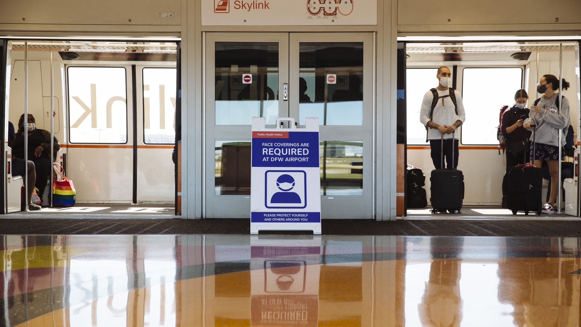 Photo of a sign that says "Masks required" outside a Skylink train with masked passengers standing