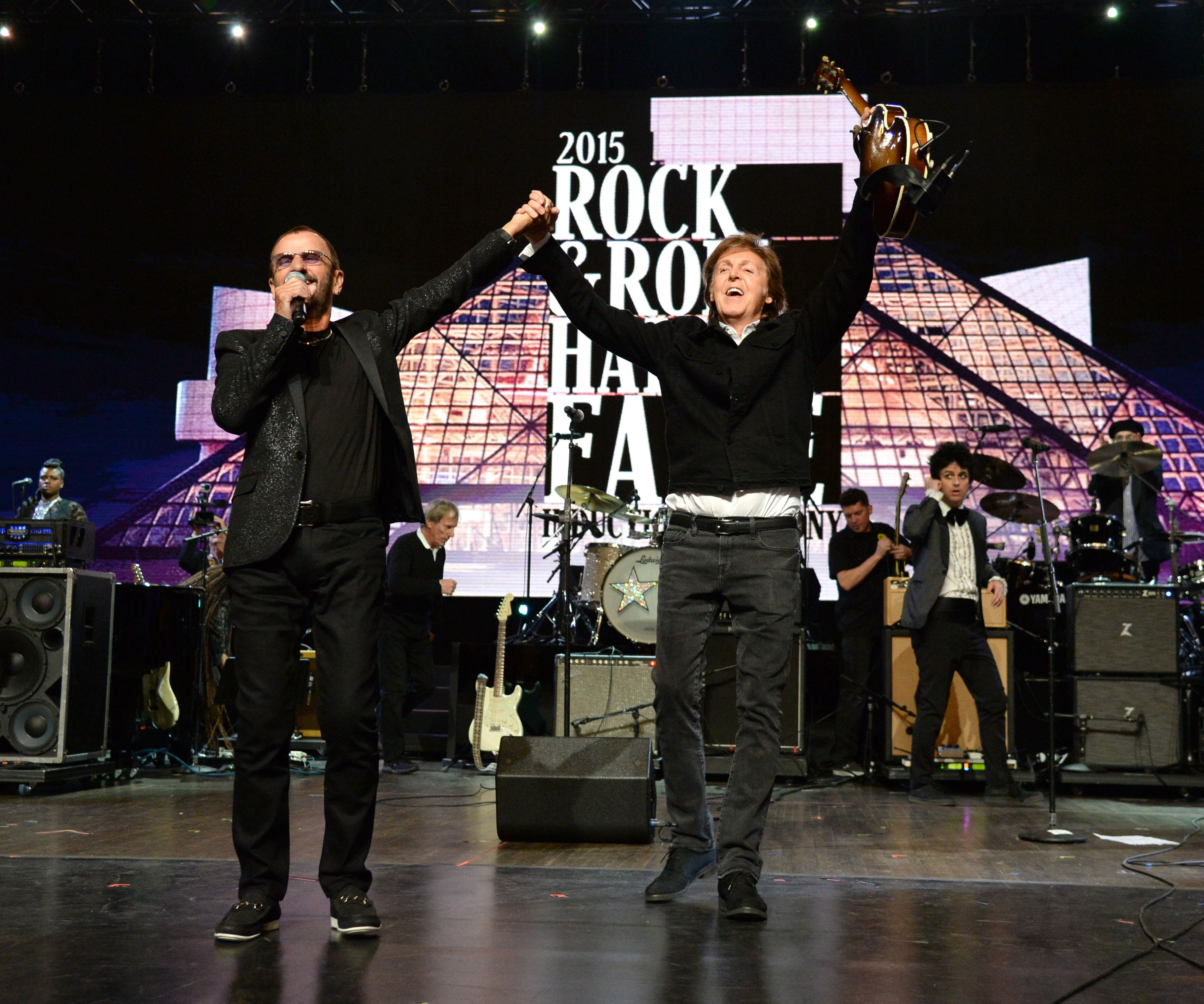 Ringo Starr and Paul McCartney raise their hands together on a Rock & Roll Hall of Fame stage. 
