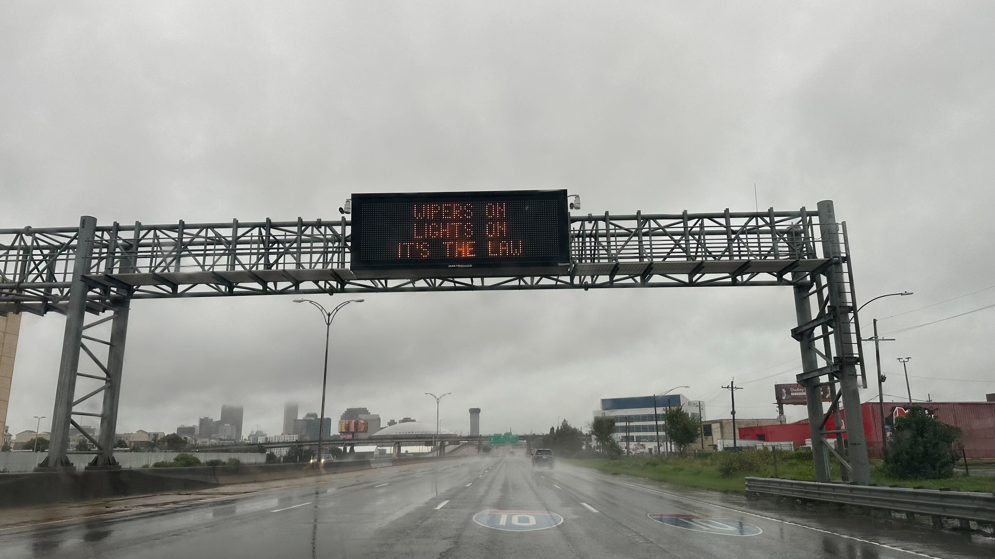 A sign hangs over I-10 saying "Wipers on, lights on."