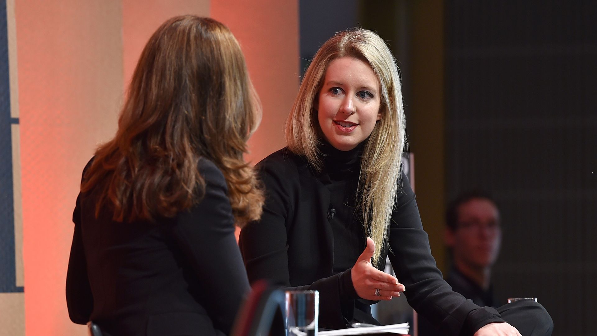 Theranos Founder and CEO Elizabeth Holmes speaks on stage in a black turtleneck. 