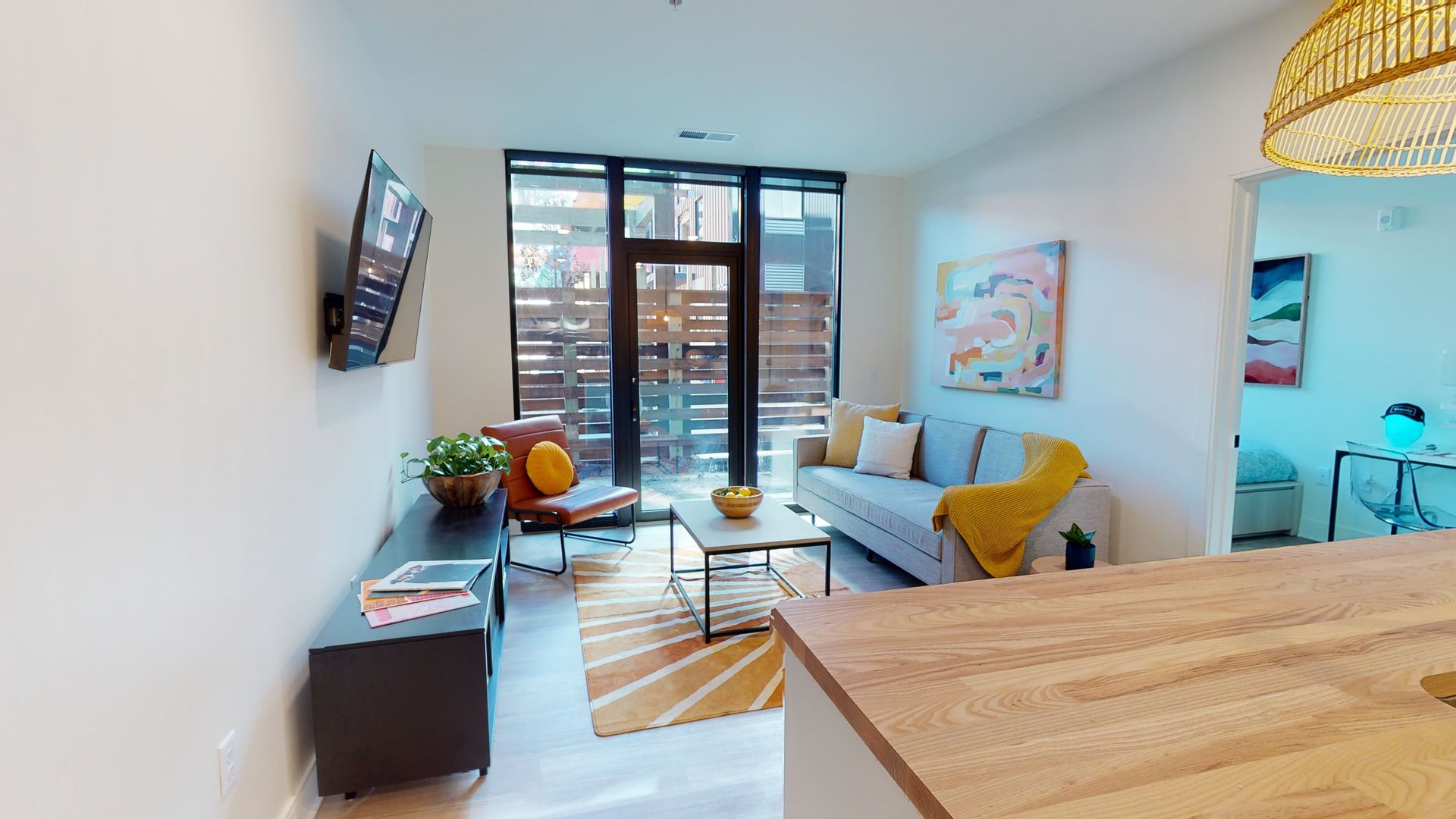 A view of a living room from the kitchen of a shared living apartment, with a mounted TV, couch, patio and coffee table