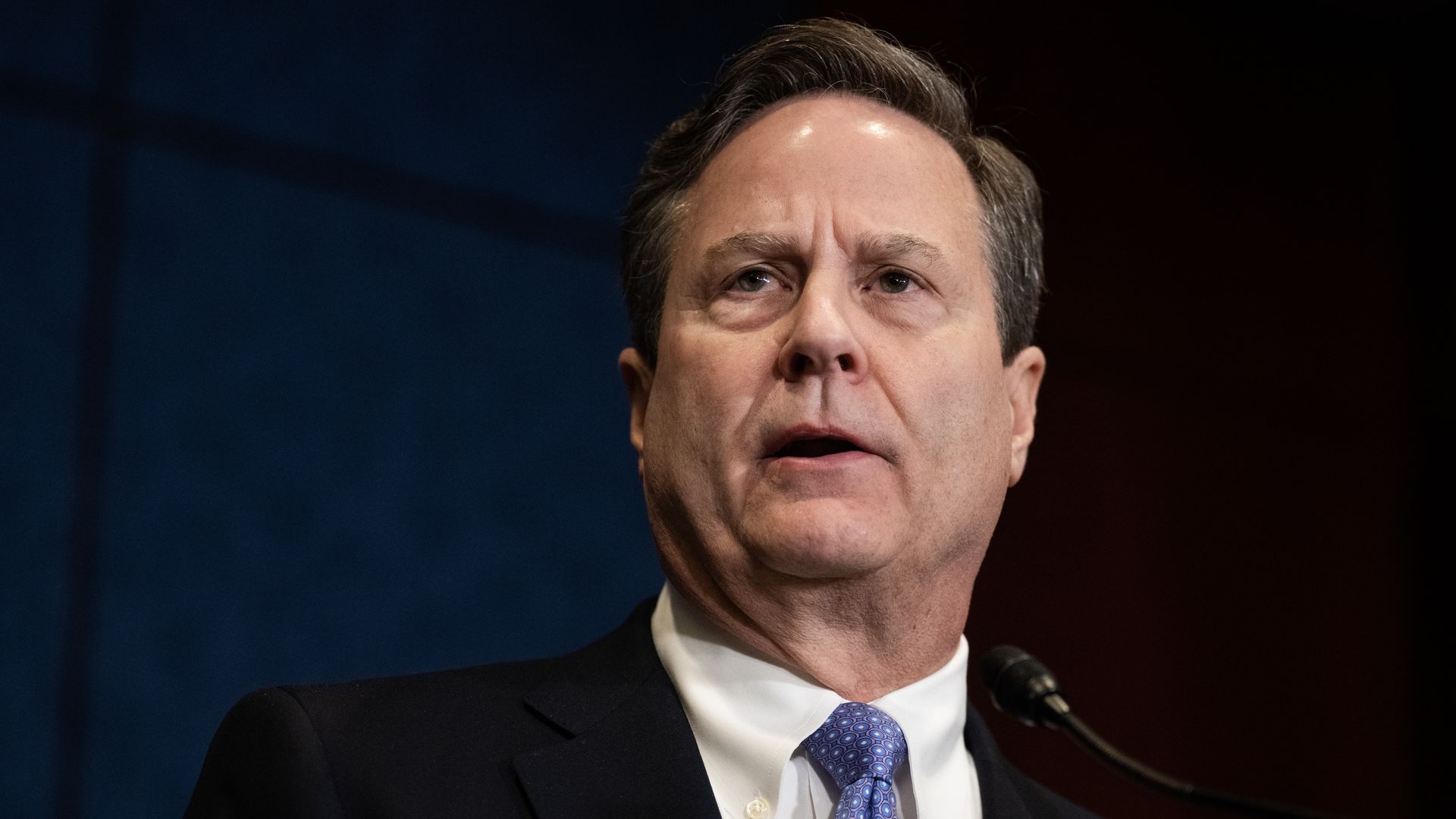 Rep. Donald Norcross wearing a black suit and speaking into a microphone in front of a blue wall.