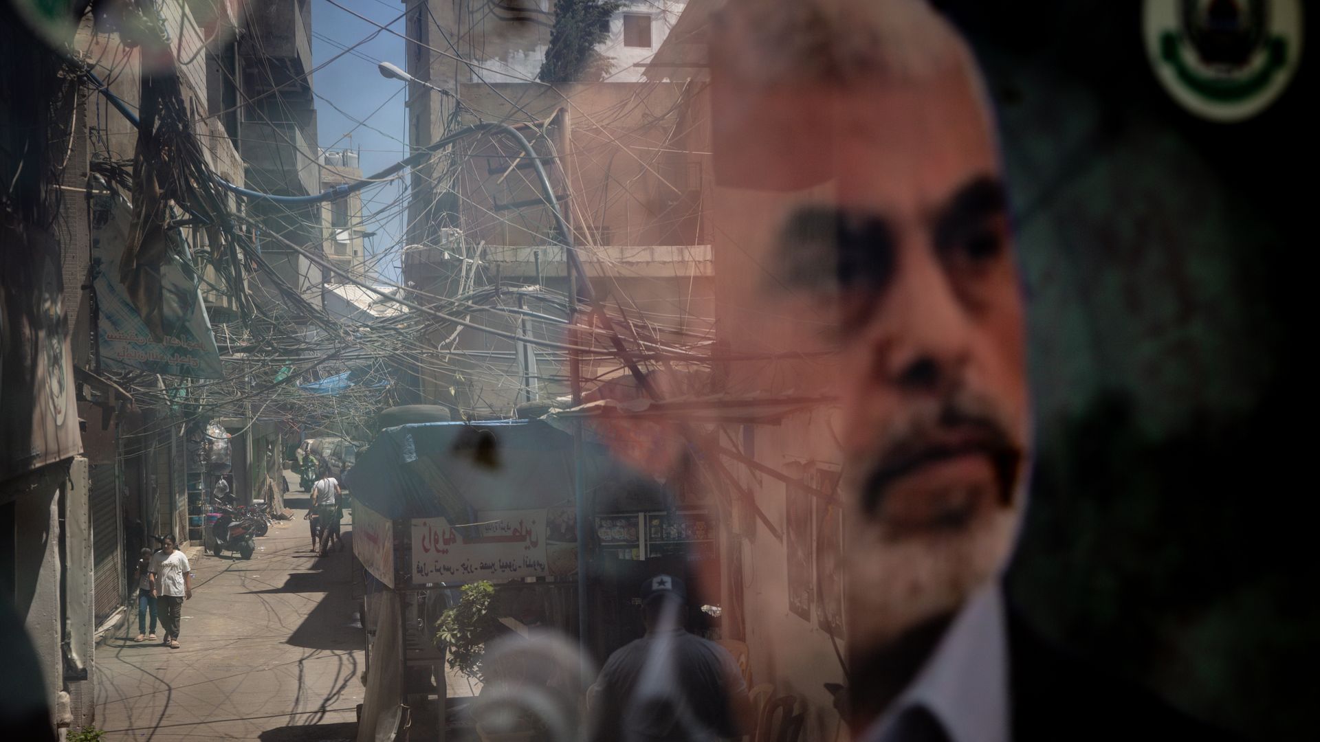 People are reflected in a window displaying a poster of newly appointed Hamas leader Yahya Sinwar in the Palestinian camp of Bourj al-Barajneh on August 08, 2024 in Beirut Lebanon. 