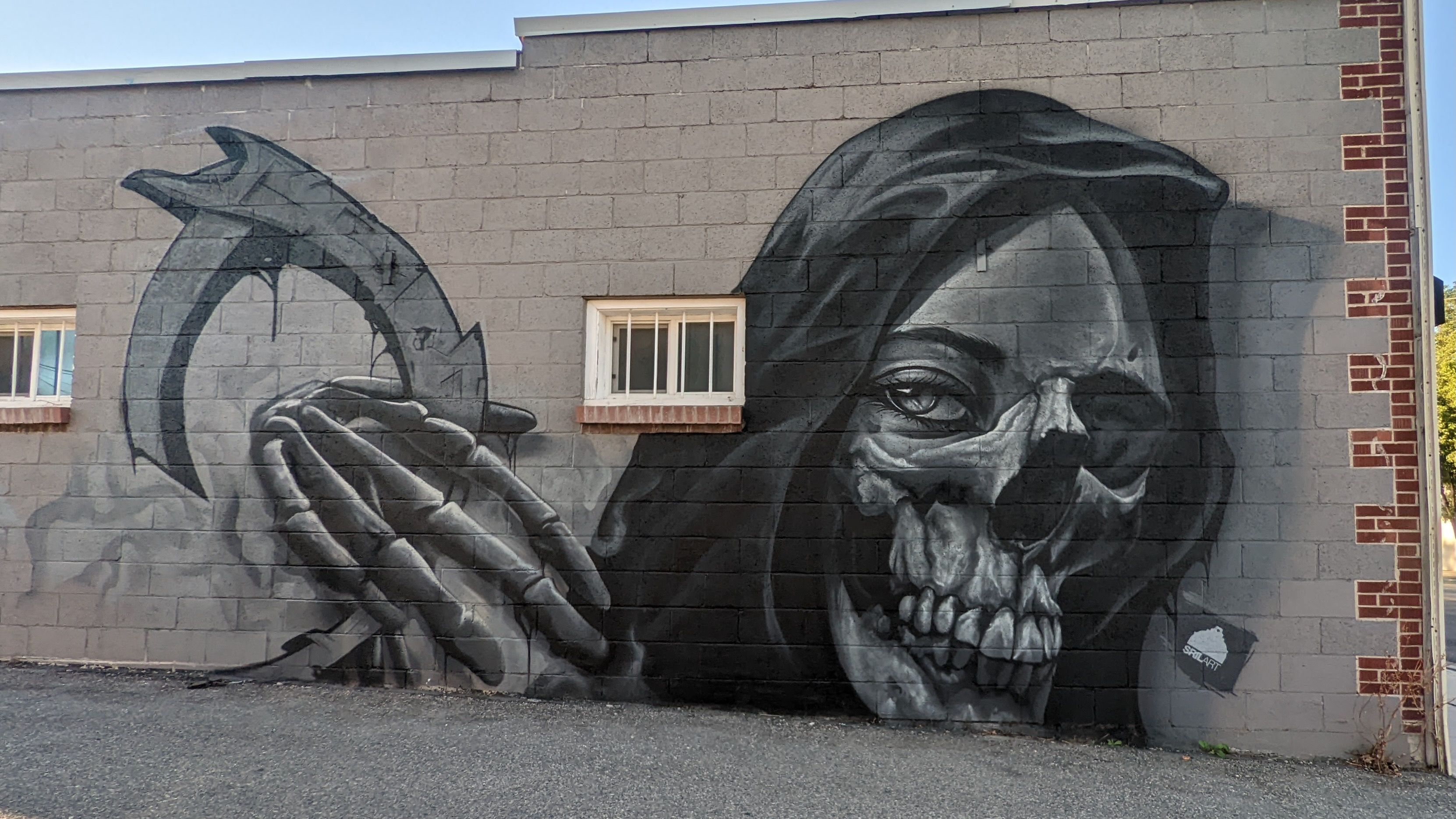 A hooded skull is painted on a brick wall.