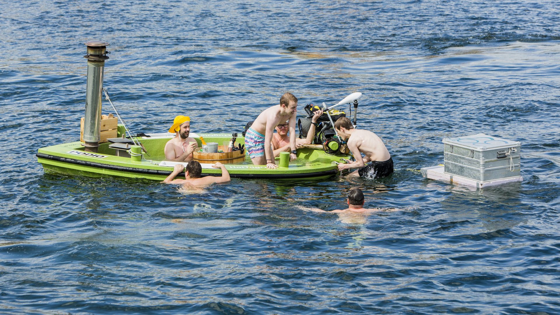 Young men sit in a floating bathtub in the water in Copenhagen’s harbor.