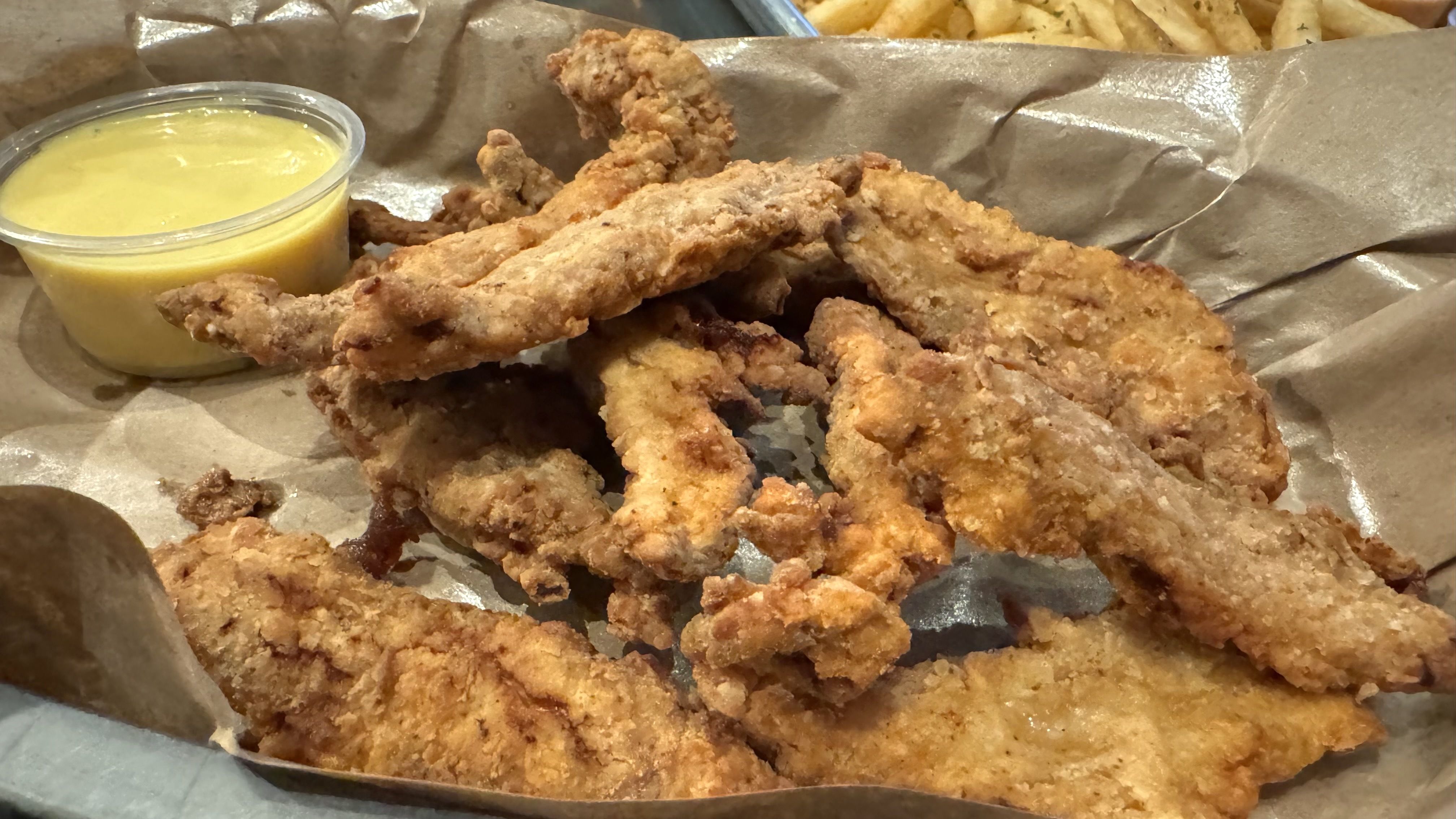 A plate of fried duck tenders with a side of honey mustard sauce. 