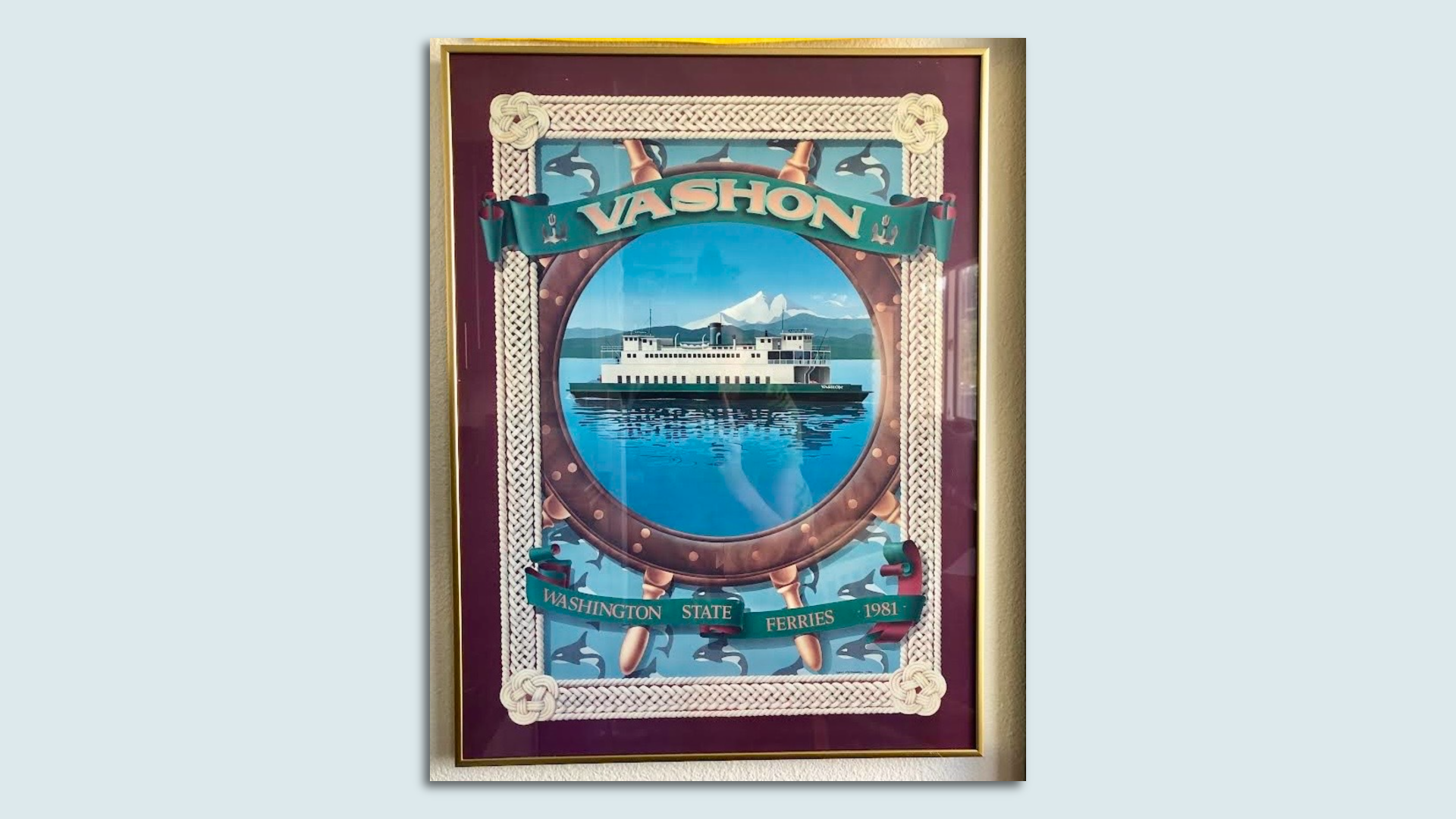 A picture of a framed poster of a ferry floating on water, with "Vashon" written above the image of the boat. Photo is mounted on a light blue background.