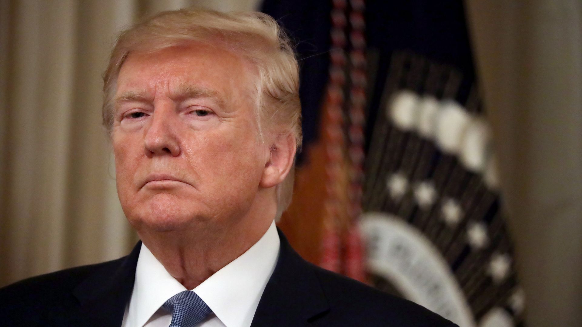 In this image, Trump stands in a suit