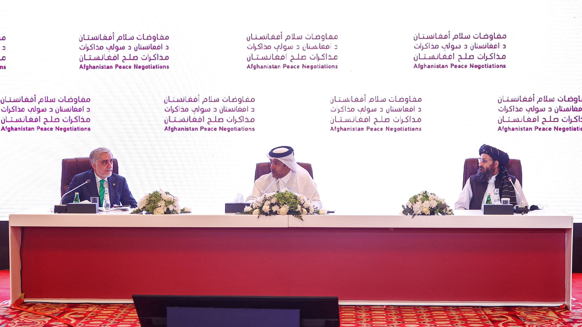 Three men seated at a conference table onstage 