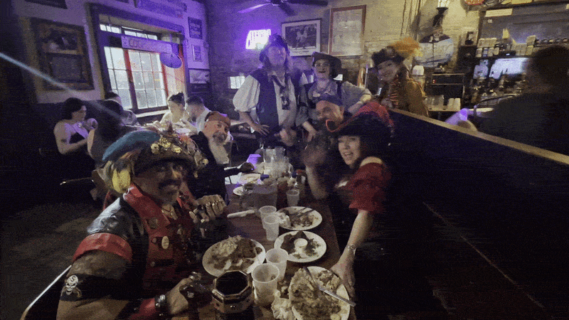 Image shows people dressed as pirates and eating and waving at a table.