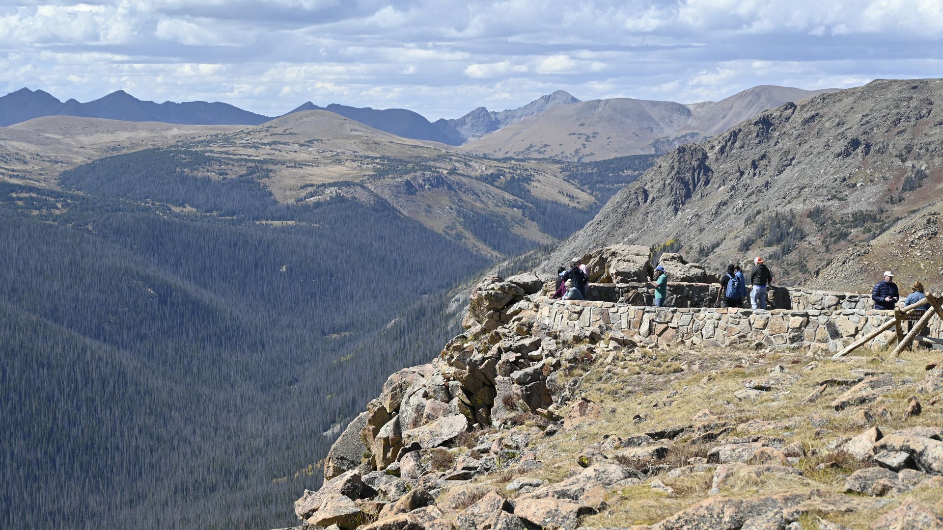 A photo of people standing on a rocky overlook with grassy mountains in the backdrop.