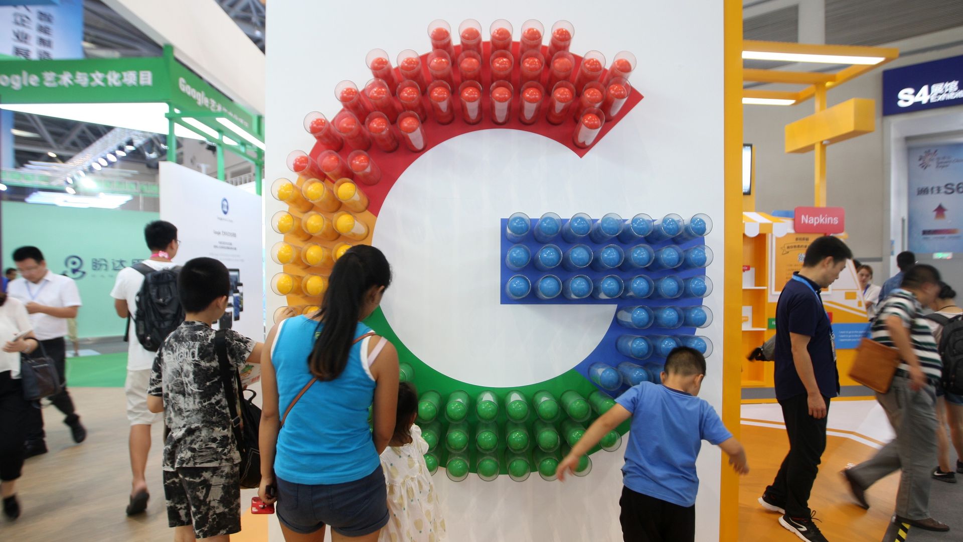 Red, yellow, green, and blue G symbolizing Google on a wall as people look on.