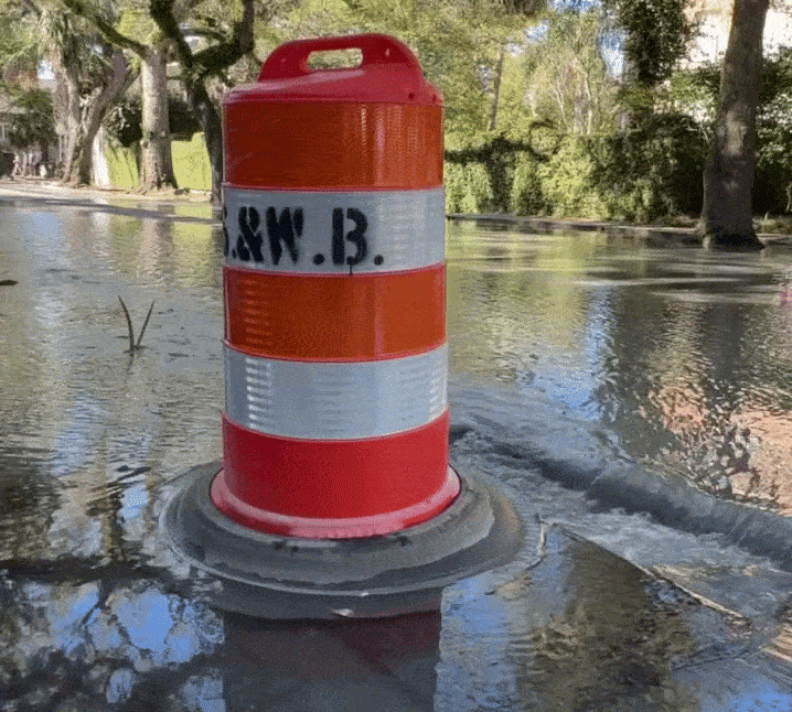 Image shows an orange construction barrel in a flooded street.
