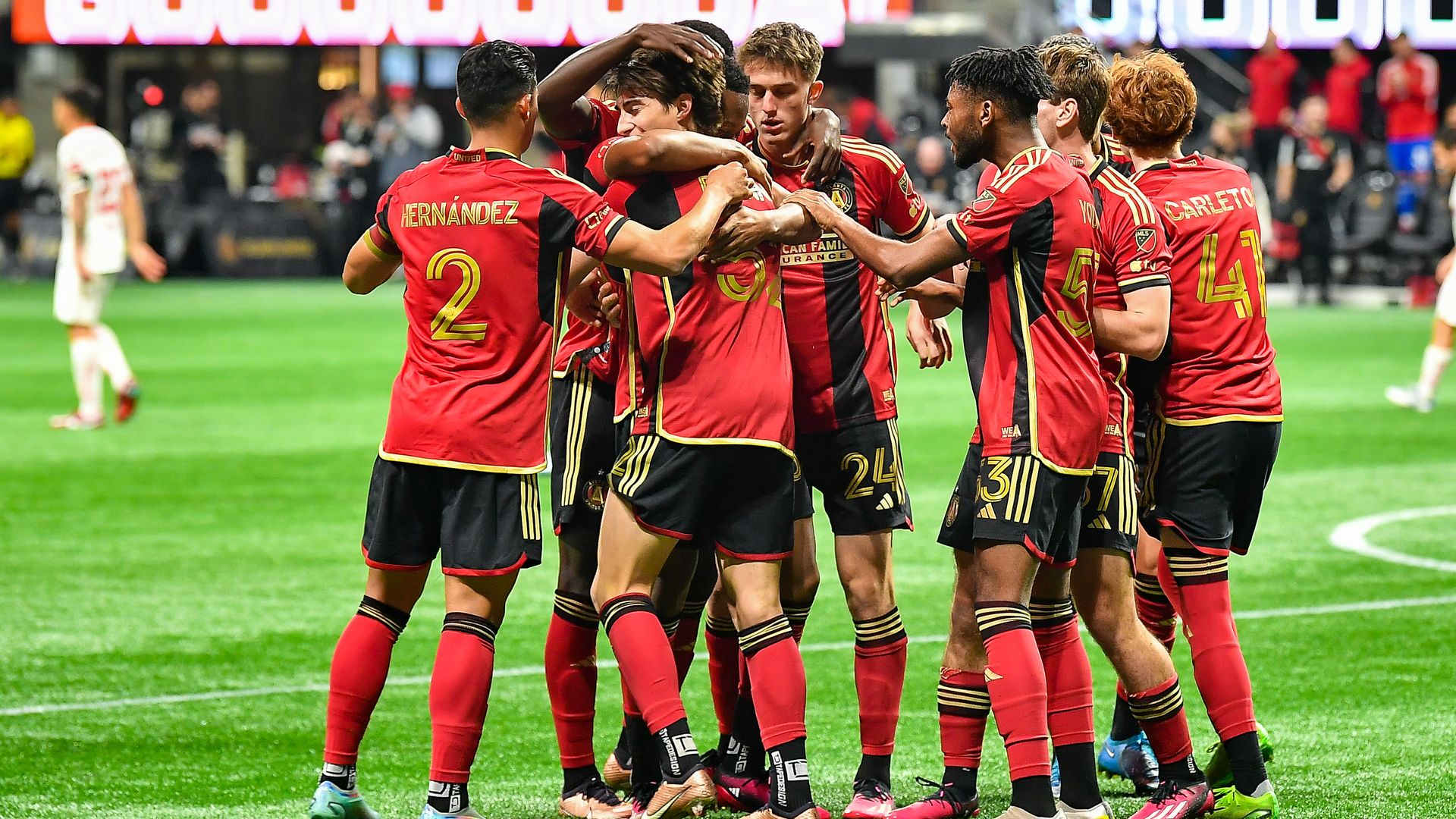 Soccer players wearing red and black kits celebrate after a player scores a goal